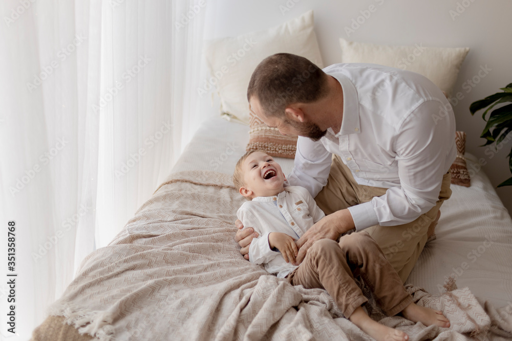 Father crouching on bed tickling his little son