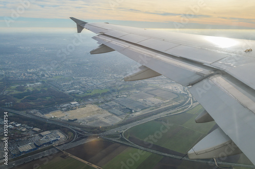 View over the clouds from the porthole of an airplane with plane wing over the Paris Airport area at take off