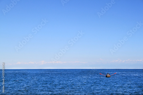 A lonely boat is sailing in bright blue water. Clear sky. Fishermen swam into the sea. Friends are resting.