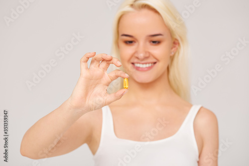  Beautiful smiling woman holding fish oil pills in her hand on a gray background. Healthy eating