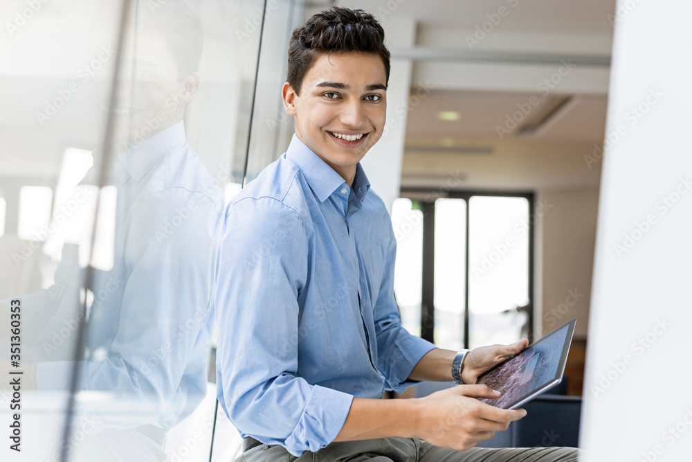 Portrait of smiling young businessman with tablet at the window in office Portrait of smiling young businessman with tablet at the window in office