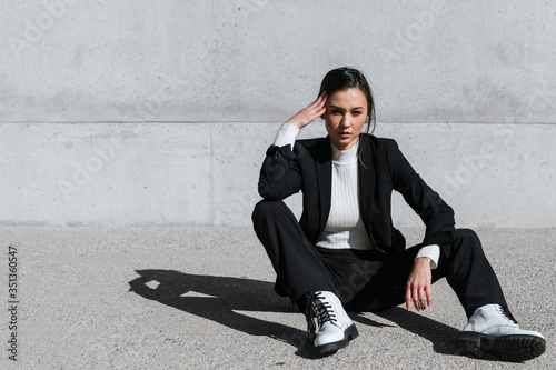 Young woman wearing black suit sitting on floor in front of concrete wall