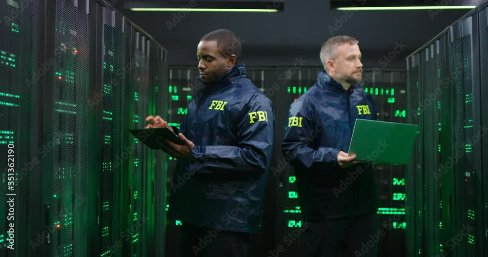 Mixed-races male FBI co-workers operating with data in server center ...