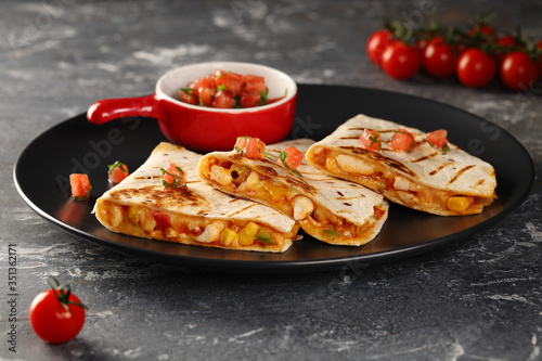 Grilled Quesadilla with chicken, cheese and vegetables. Served on a black plate with sauce of fresh tomatoes and herbs.