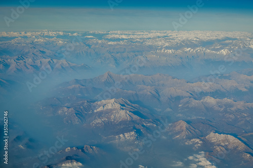 View over the clouds from the porthole of an airplane of italian alps mountains