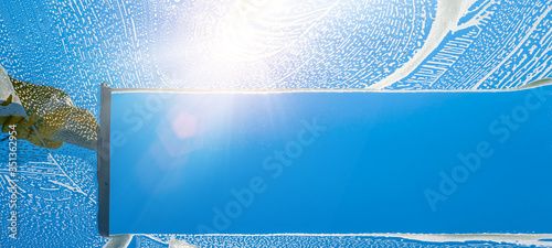Window cleaner cleaning window with squeegee and wiper on a sunny day with a bright blue sky