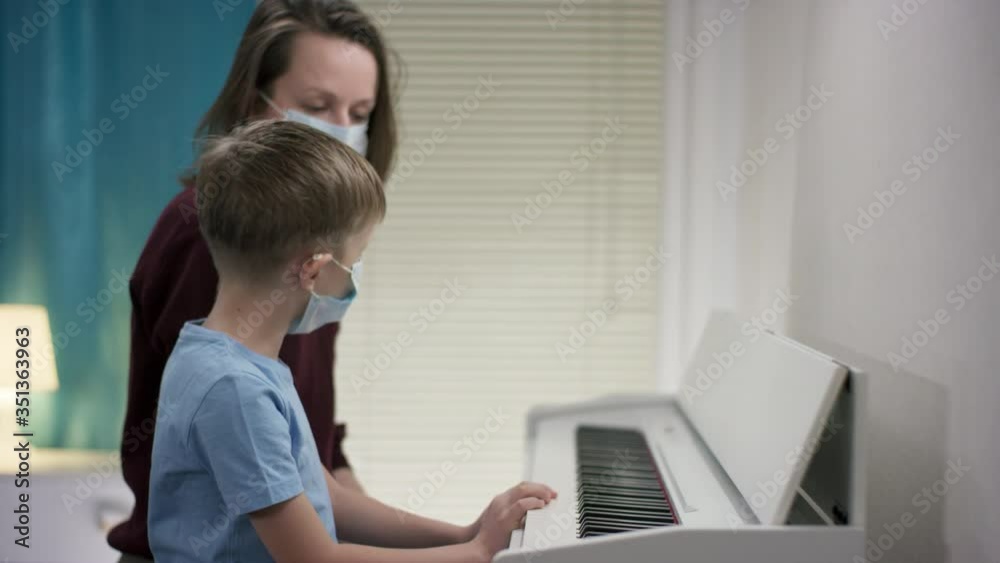 Sideview closeup shooting of a mother in a red coat giving her young child in a blue tee a lesson on composing music on piano during isolation Sideview closeup shooting of a mother in a red coat giving her young child in a blue tee a lesson on composing music on piano during isolation
