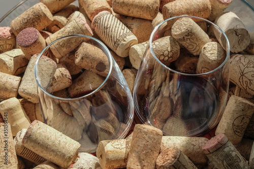 Two wine glasses with red wine among wine corks. Reflection of corks in wine.