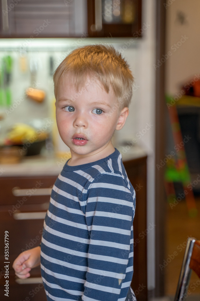 Little cute blond boy in kitchen looks carefully out window close up Little cute blond boy in kitchen looks carefully out window close up