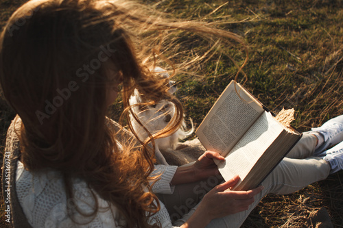 Top view of a girl sitting under a tree on the grass and reading book. Attractive woman's golden and fluttering hair in the wind. Outdoor activities, a girl and her cute little dog are reading a book.