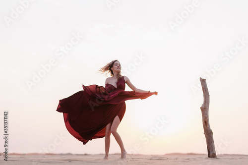 Silhouette of a girl in a red dress at sunset in the desert 