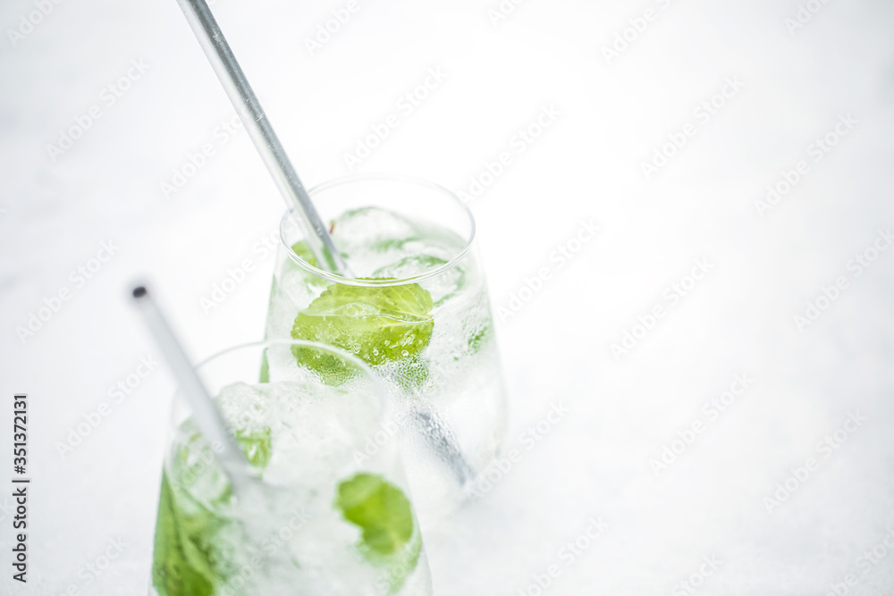 Beautiful glass of water or mojito with lime and mint cocktail on the gree background and white table summer vibe and atmosphere Beautiful glass of water or mojito with lime and mint cocktail on the gree background and white table summer vibe and atmosphere