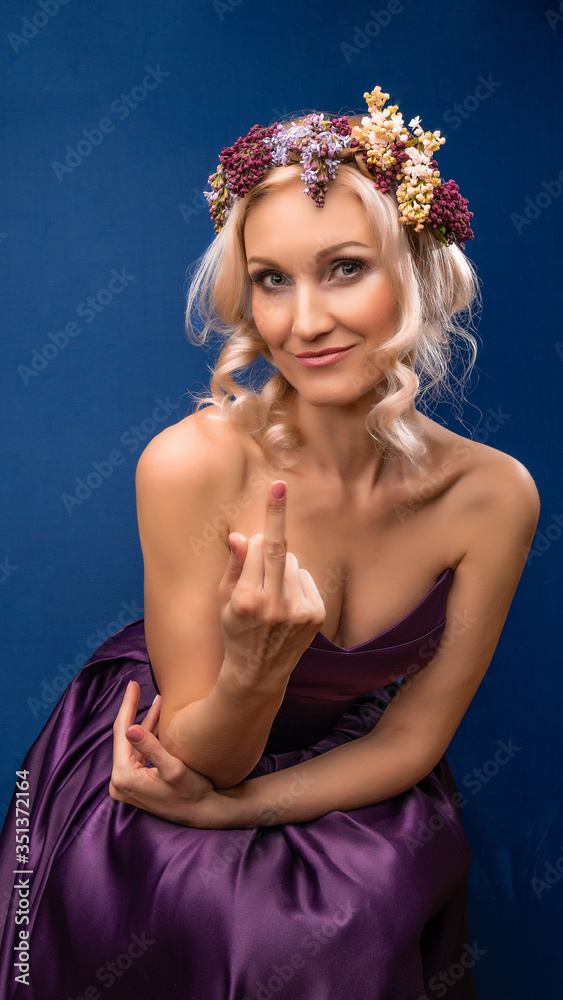 Lovely young beautiful in a lilac wreath with a charismatic appearance blooms on a blue background, with, shows finger