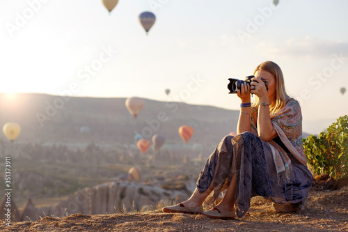 Woman photographer takes pictures of flying hot air balloon at dawn in Cappadocia