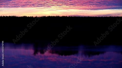 A fantastic picture of a sunset on the lake with a mirror reflection of a shining continuous cloud of mixed colorful purple tones in the blue ripples of the current.Contrast of black and gold.Russia