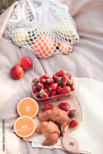 Strawberry in box with croissants and fruits on cloth outdoors closeup. Holidays. Summer season.