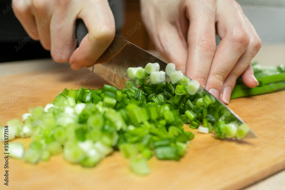 Women's hands cut green onions with a knife on a wooden Board close up Women's hands cut green onions with a knife on a wooden Board close up