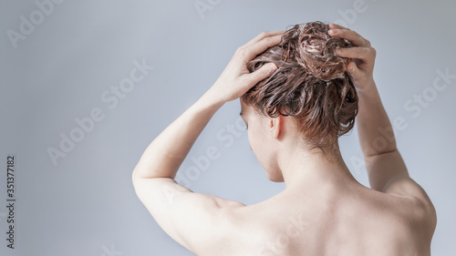 Girl lathers her head with shampoo on a blue background view from the back. Hair care concept