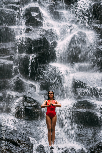 A woman does yoga at a waterfall. Healthy lifestyle. The concentration of the body. A woman does yoga in Bali. A woman meditates in nature. Meditation at the waterfall. Young woman practicing yoga