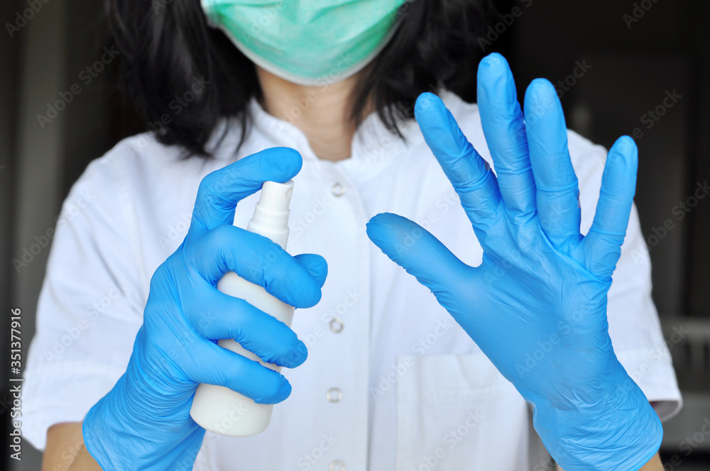 The concept of protection against bacteria and viruses. Woman wearing surgical face mask and gloves,protective against influenza sickness, holding white spray bottle with alcohol for disinfection The concept of protection against bacteria and viruses. Woman wearing surgical face mask and gloves,protective against influenza sickness, holding white spray bottle with alcohol for disinfection