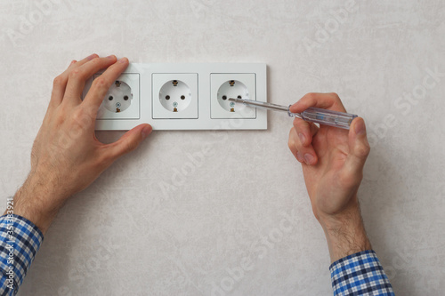 Hand of electrician using phase tester screwdriver to repair wall socket