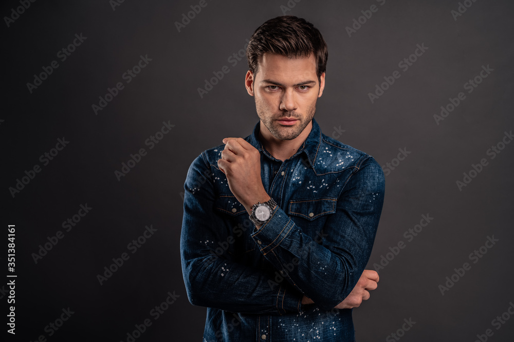 Totally perfect. Handsome young man keeping hand on chin and looking at camera while standing against grey background Totally perfect. Handsome young man keeping hand on chin and looking at camera while standing against grey background