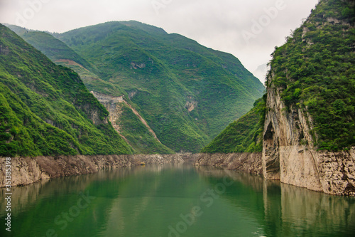 Guandukou, Hubei, China - May 7, 2010: Wu Gorge in Yangtze River: the deep canyon filled with emerald green water between green forested covered mountains, and belt of brown rock cliffs near water.