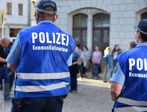 Polizeibeamter mit blauer Weste und Aufschrift: "Kommunikationsteam " auf einer Demo