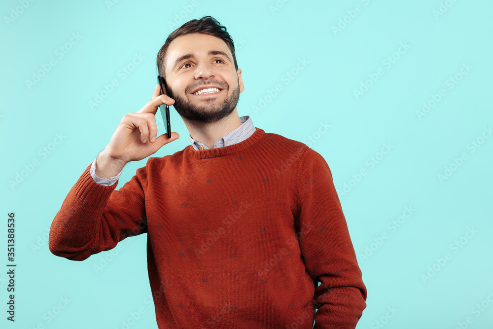 Gleeful bearded young man in casual outfit talk on smartphone over cyan background. Gleeful bearded young man in casual outfit talk on smartphone over cyan background.