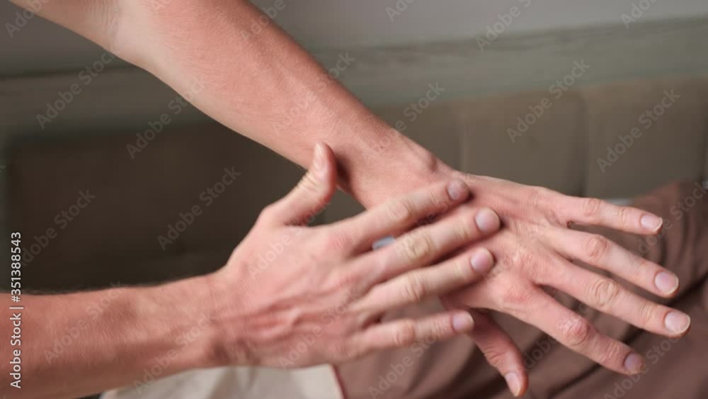 sporty man stretches muscular hand and massages fingers against brown bed in hotel room in morning extreme close view sporty man stretches muscular hand and massages fingers against brown bed in hotel room in morning extreme close view