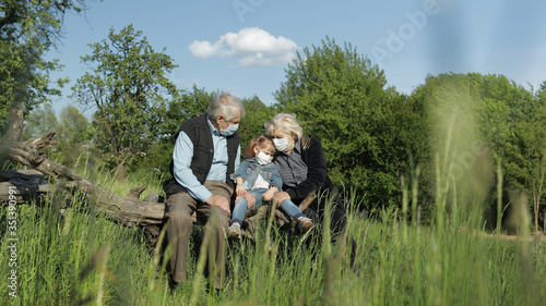 Grandparents with granddaughter in medical masks in park. Coronavirus quarantine