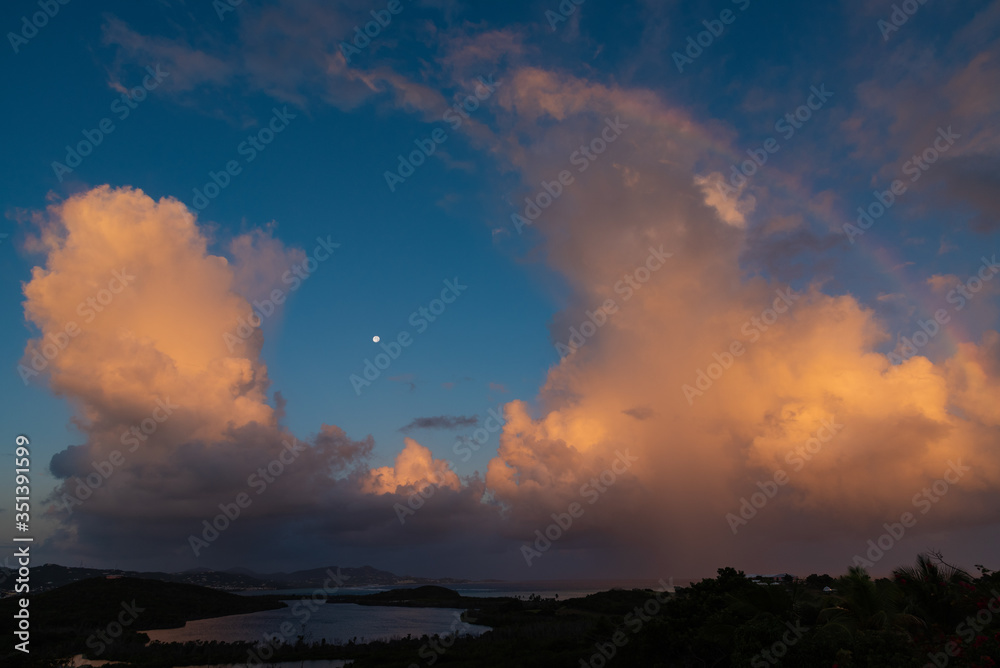 island sunrise with clouds, moon, and rainbow