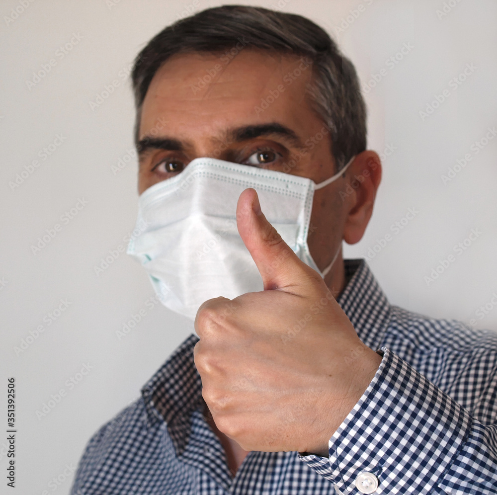 portrait of medium age man wearing a medical mask doing thumbs up gest over white background portrait of medium age man wearing a medical mask doing thumbs up gest over white background