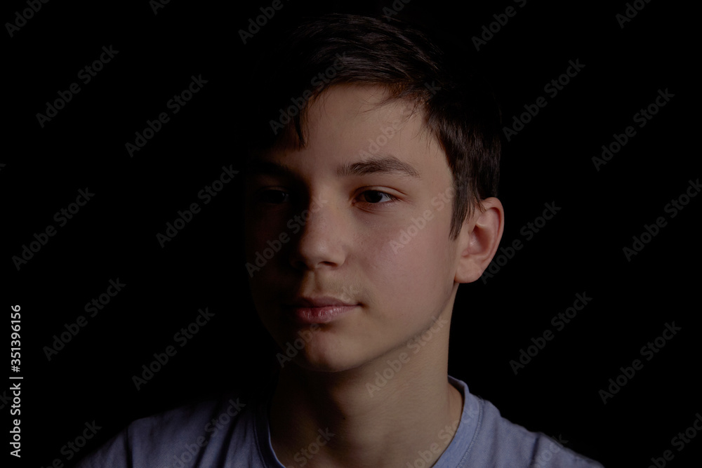 Portrait of a teenager on a black background. The boy has dark hair Portrait of a teenager on a black background. The boy has dark hair
