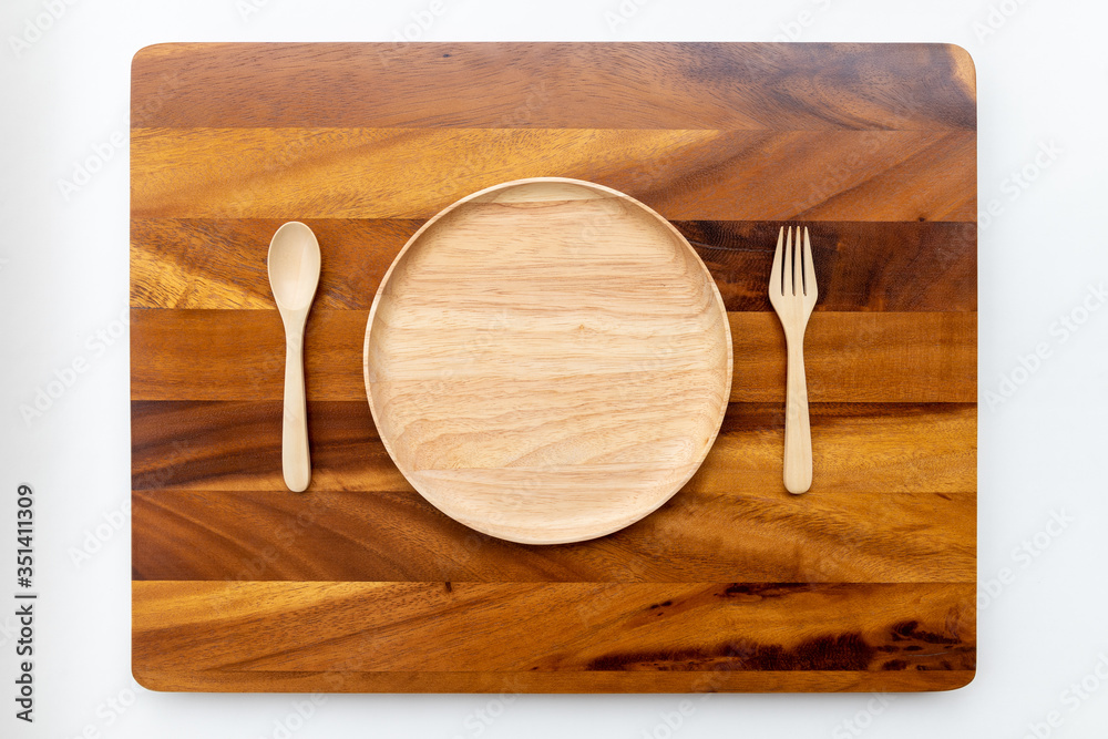 Round plates made from rubber wood with natural colors, polished and lacquered, placed on a wooden chopping block made of acacia tree, with spoons and forks, and with a white background.
