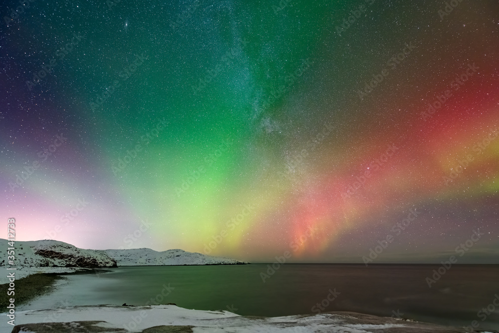 colorful northern light aurora borealis with purple, red, green and blu flames over the sky in iceland in a beach in