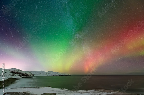 colorful northern light aurora borealis with purple, red, green and blu flames over the sky in iceland in a beach in
