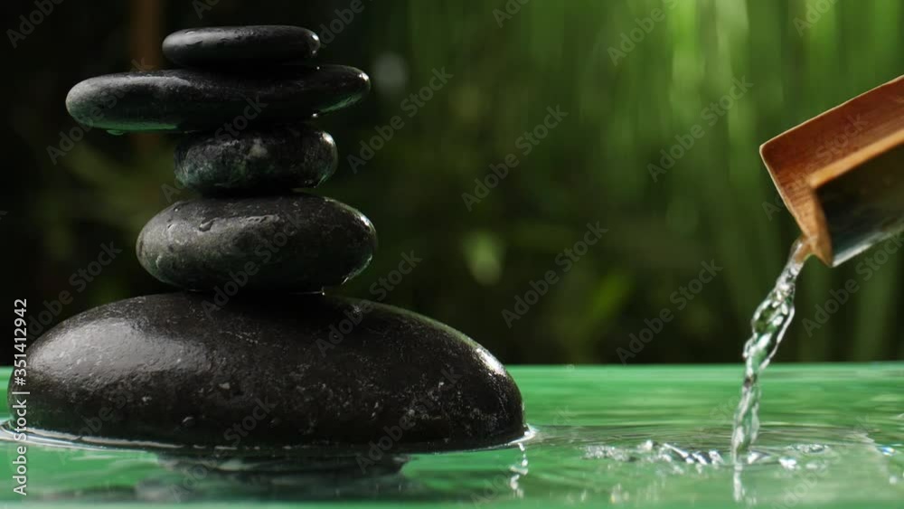 Water pouring from bamboo into lake with stack of zen stones in oriental garden