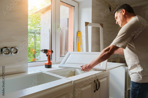 Middle-aged Caucasian man holds the door of the kitchen cabinet, preparing for the process of custom installation in his own house. Quarantine activity, repair concept