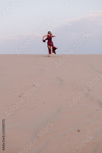 Girl in red dress with cloth in the wind in the desert