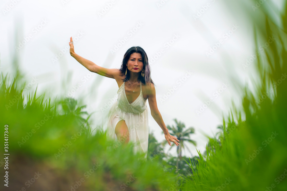 mind and body connection with nature - middle aged attractive and happy Asian Korean woman in Summer dress enjoying idyllic tropical destination dancing free