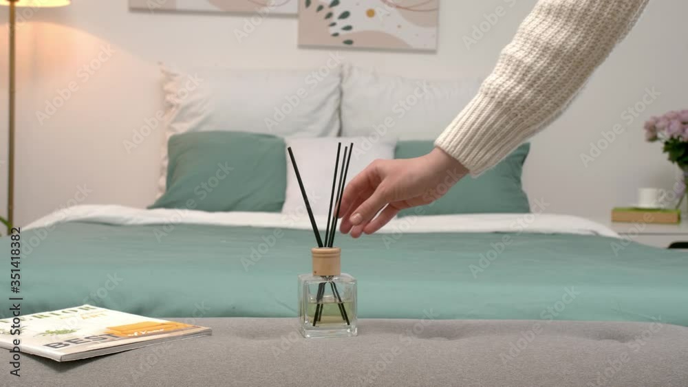 Woman putting air reed diffuser on bedside bench in room