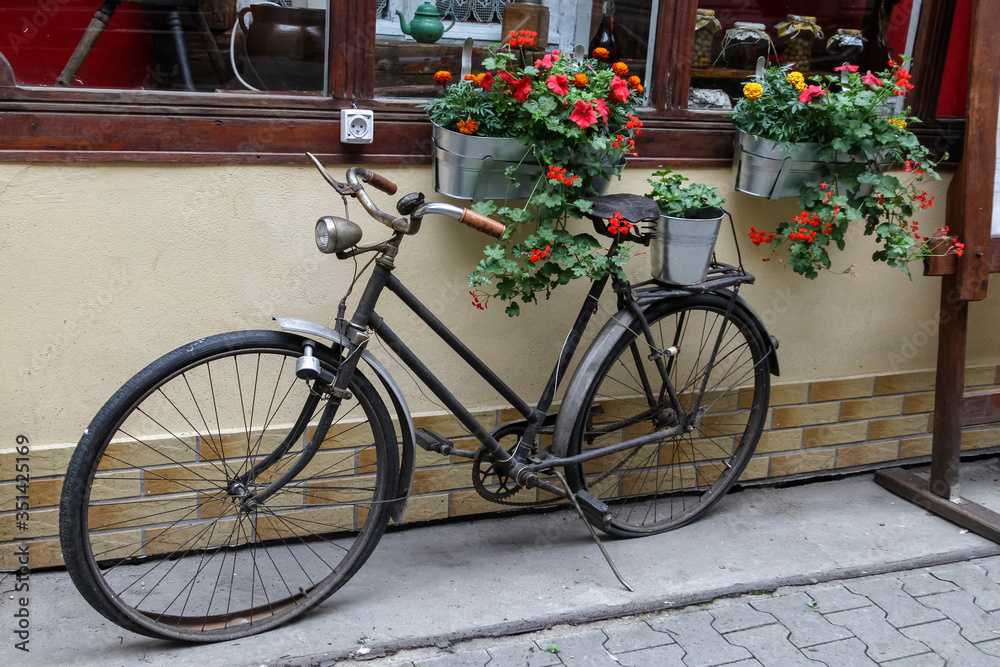 Old black bike near the cosy cafe with red and orange flowers