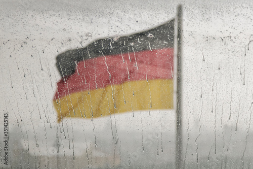 German flag on a blurred background behind glass in the rain, a sad dramatic day for Germany