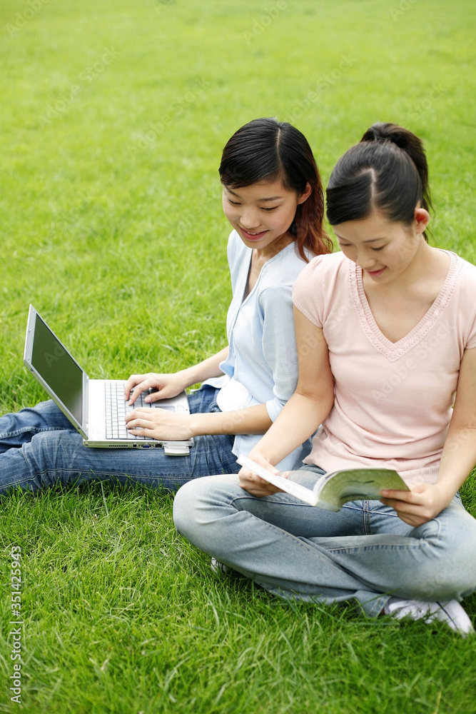 Students reading book and using laptop Students reading book and using laptop
