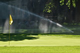 A sprinkler's spray catches the sun while watering a golf course green in Carmel, Indiana