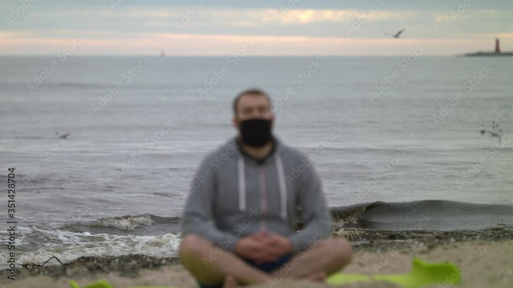 Man with Beard and Face Mask Meditating on Seashore at Dusk - Wide Rack Focus Shot Man with Beard and Face Mask Meditating on Seashore at Dusk - Wide Rack Focus Shot
