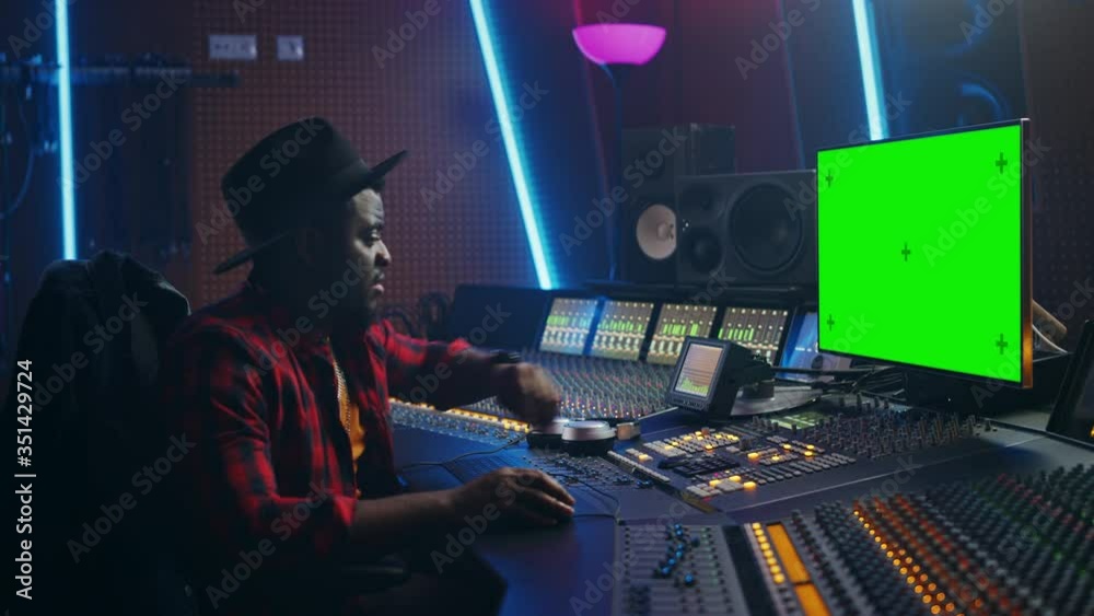 Stylish Audio Producer Working in Music Record Studio, Uses Green Screen PC, Mixer Board Equalizer and Control Desk to Create New Hit Track and Song. Creative Black Artist Musician. Side View Portrait Stylish Audio Producer Working in Music Record Studio, Uses Green Screen PC, Mixer Board Equalizer and Control Desk to Create New Hit Track and Song. Creative Black Artist Musician. Side View Portrait