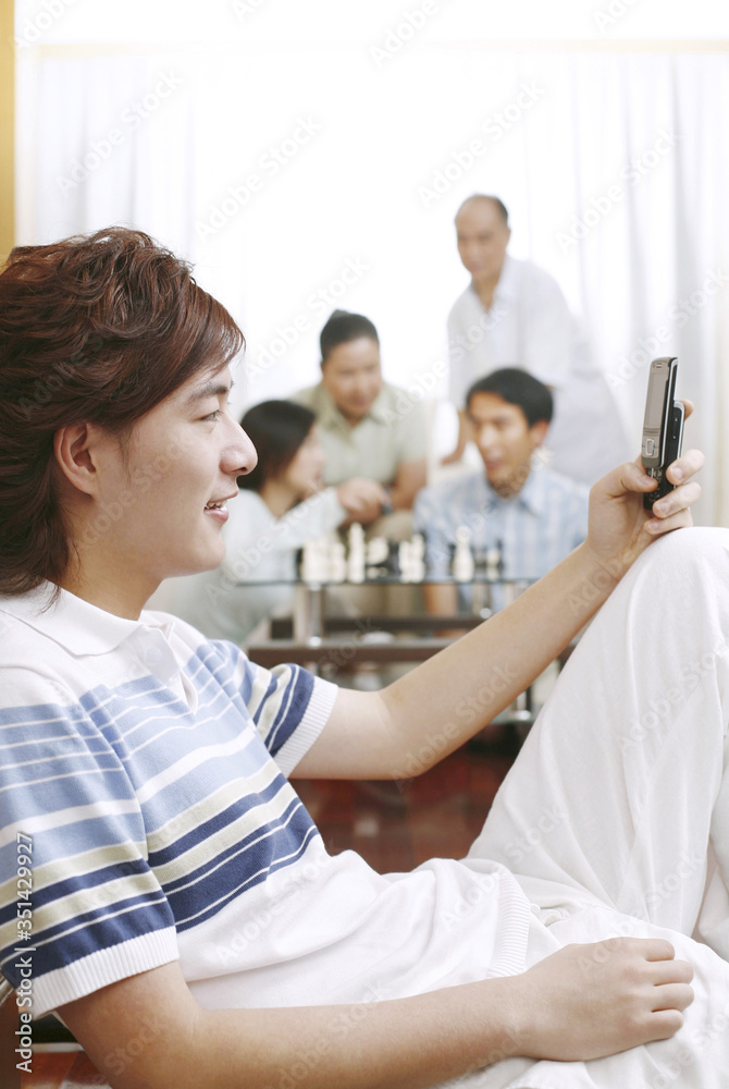 Man text messaging on the phone with people playing chess game in the background Man text messaging on the phone with people playing chess game in the background