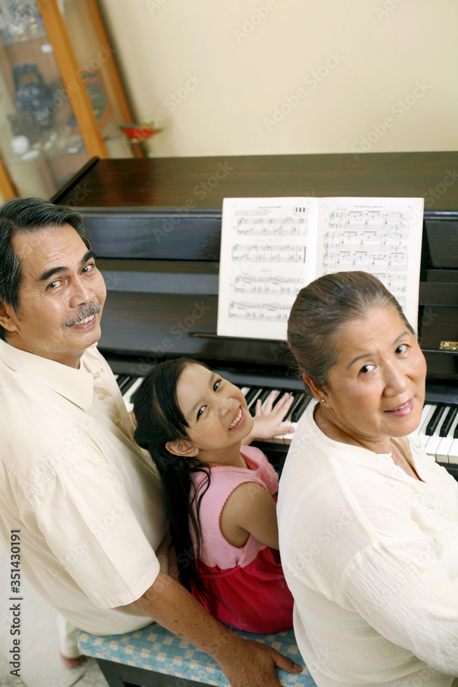 Fototapeta premium Senior man and woman playing piano with girl